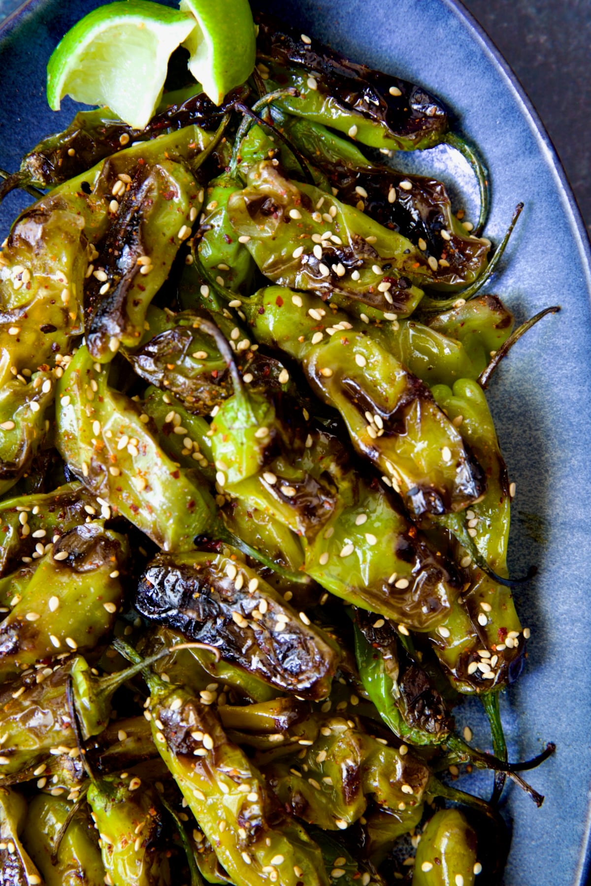 Blistered Shishito Peppers on blue oval platter garnished with sesame seeds.