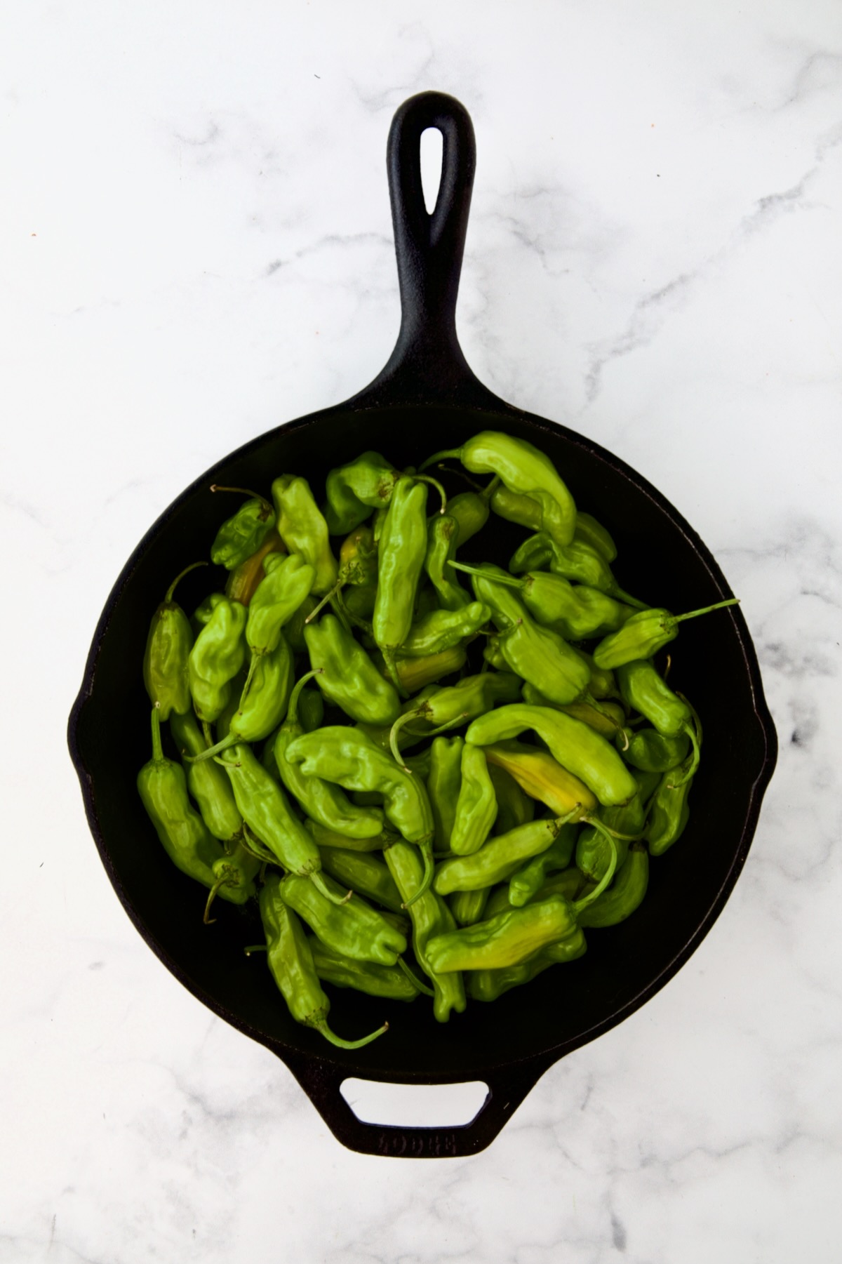 Shishito peppers in black cast iron skillet before being blistered.