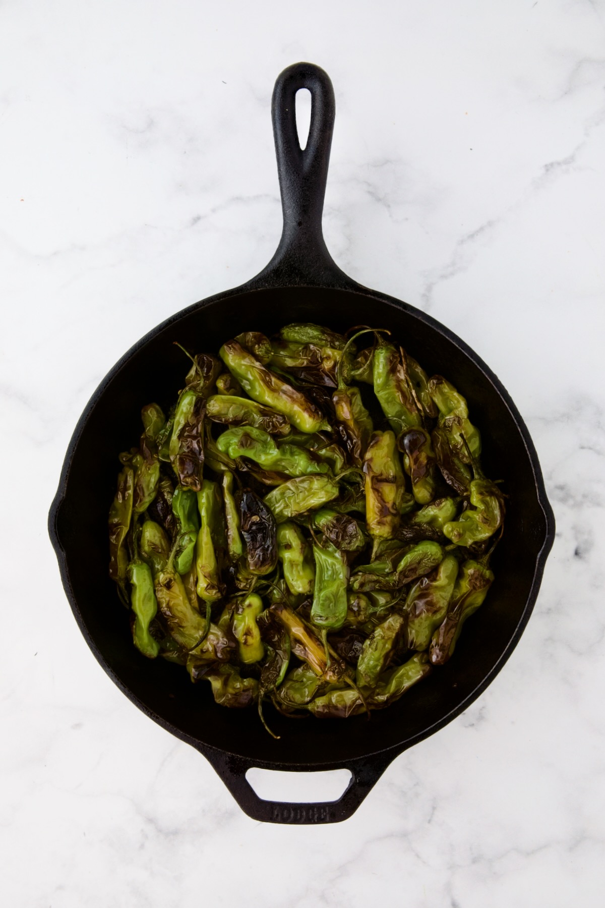 Shishito peppers in black cast iron skillet after being blistered.