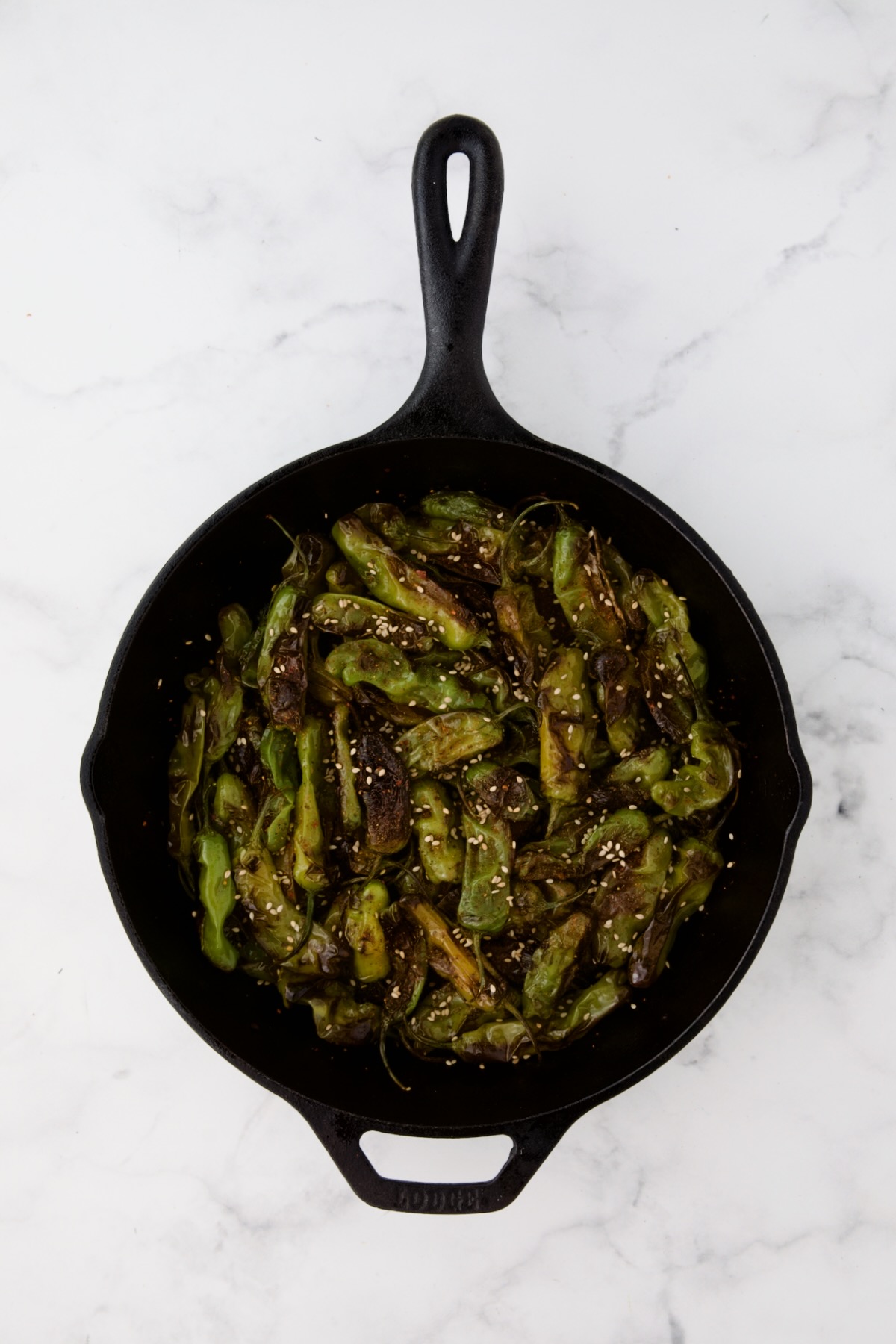 Shishito peppers in black cast iron skillet after being blistered with Togarashi seasoning and sesame seeds added.