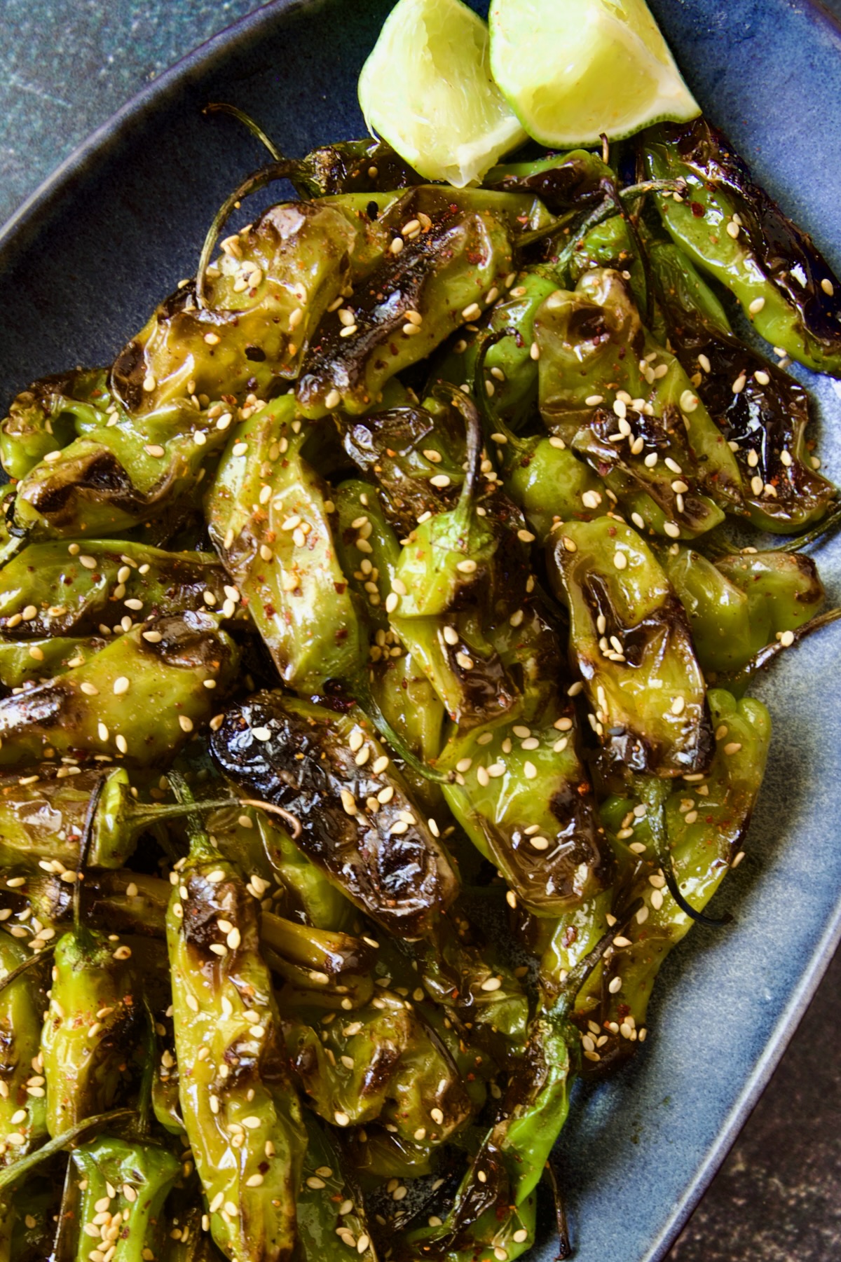 Blistered Shishito Peppers on blue oval platter garnished with sesame seeds.