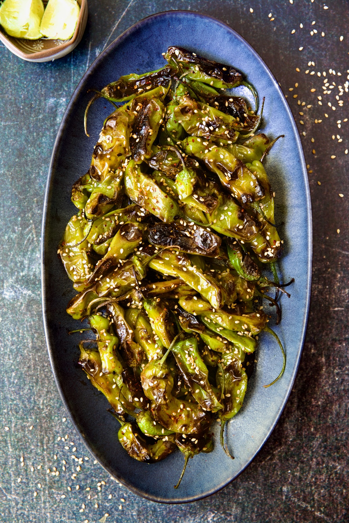 Blistered Shishito Peppers on blue oval platter garnished with sesame seeds.