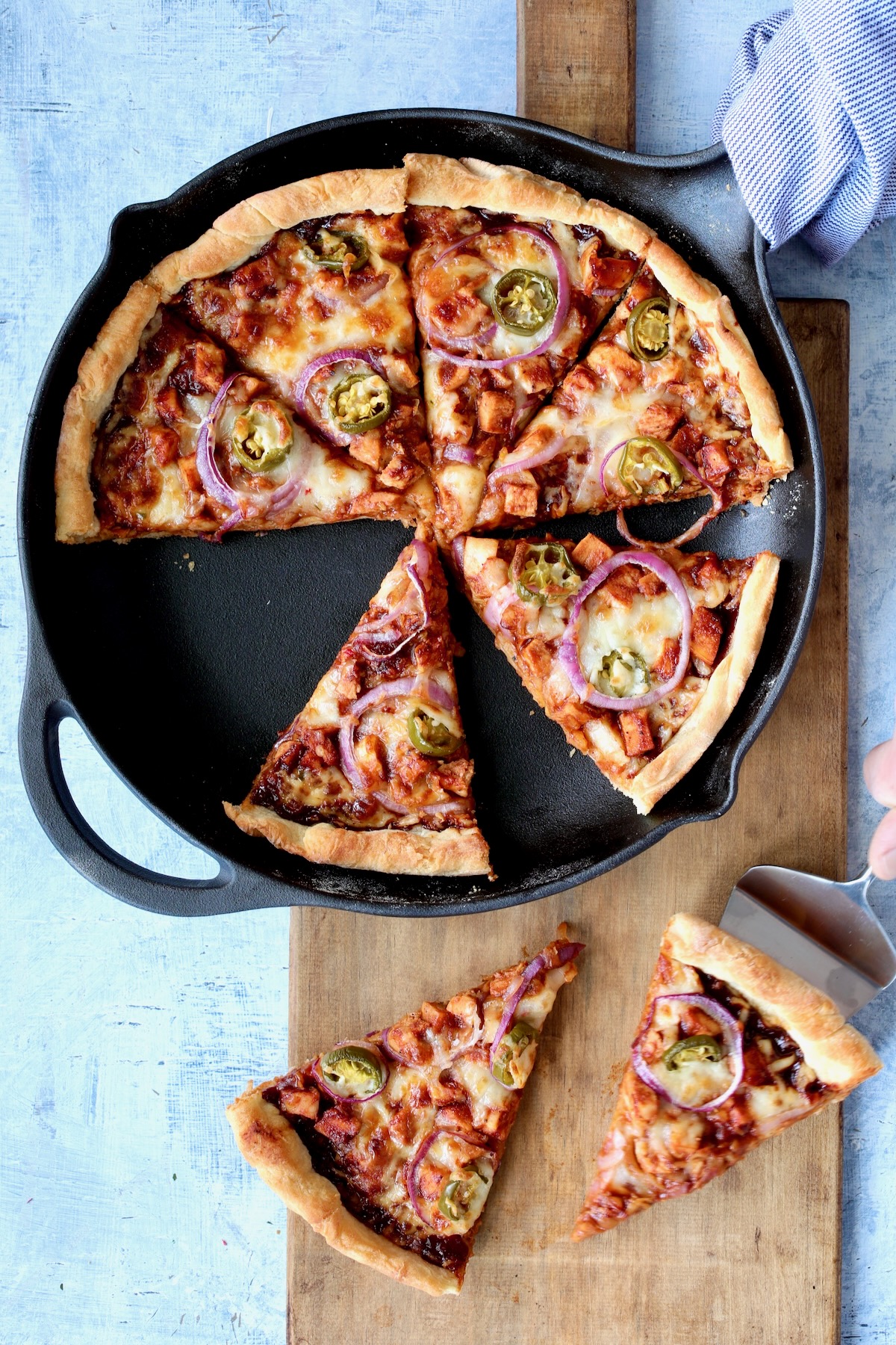 Topped pizza in cast iron skillet after being baked and cut into wedges.