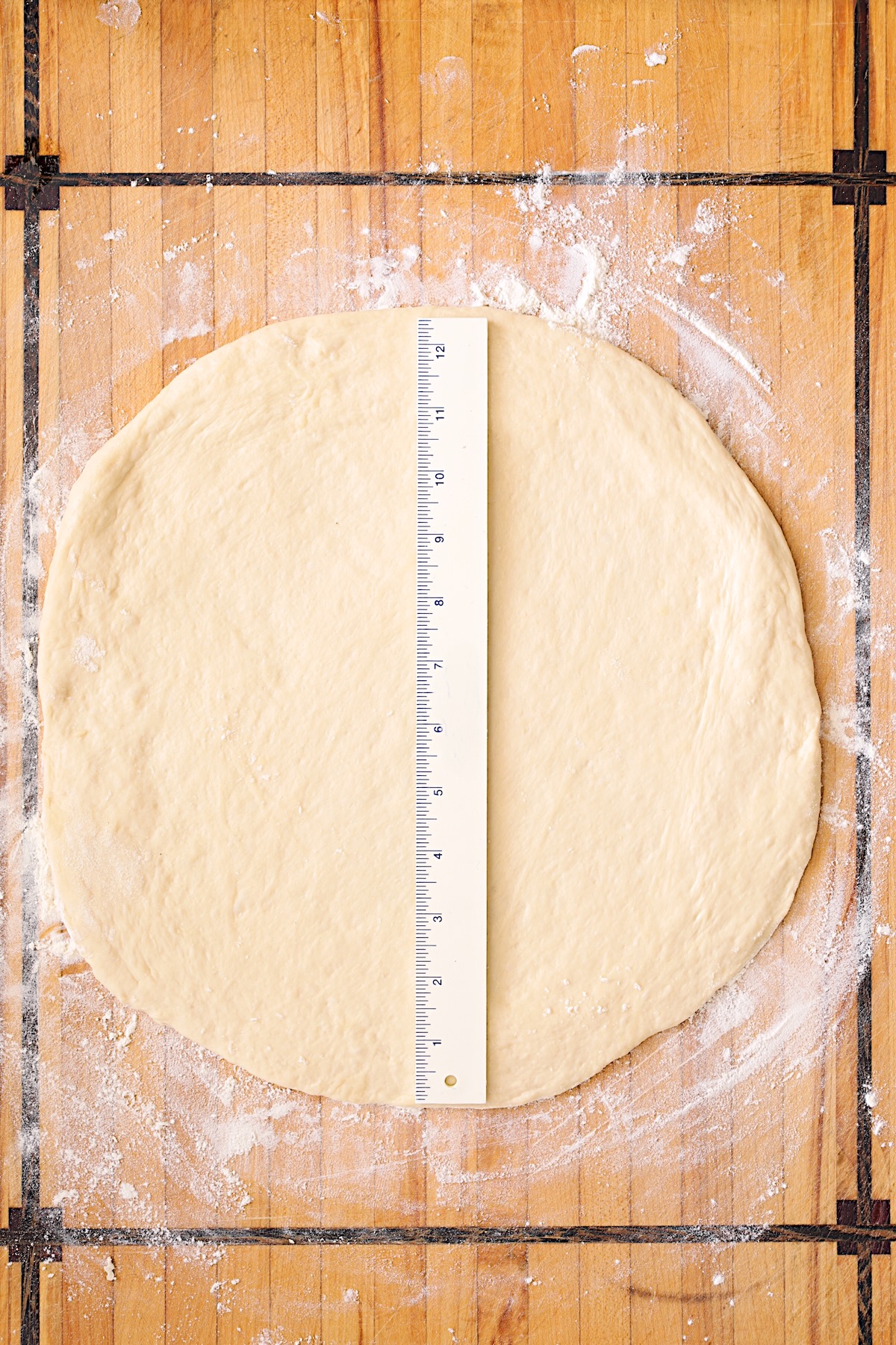 Rolled out pizza dough on wood cutting board with ruler on it to demonstrate the size.