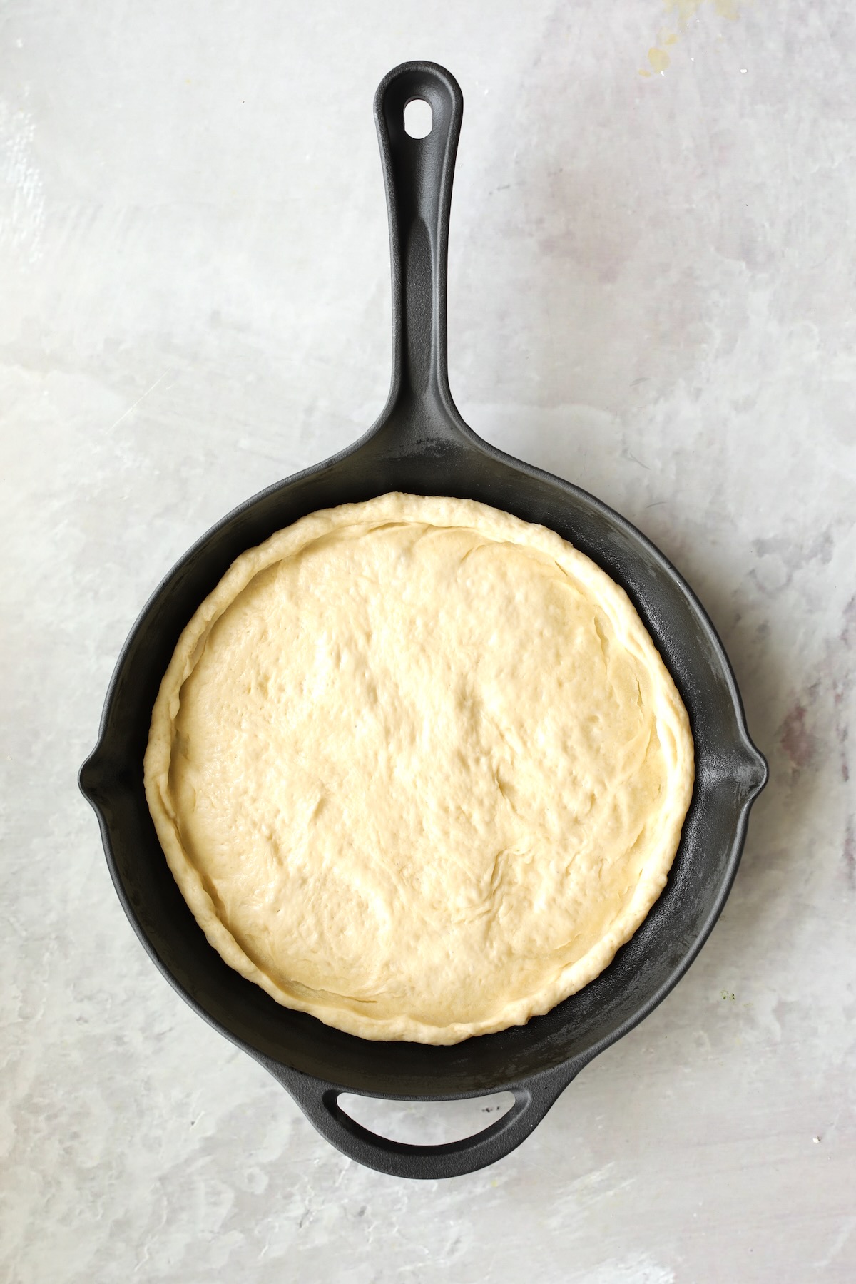 Pizza dough in cast iron skillet before toppings are added.
