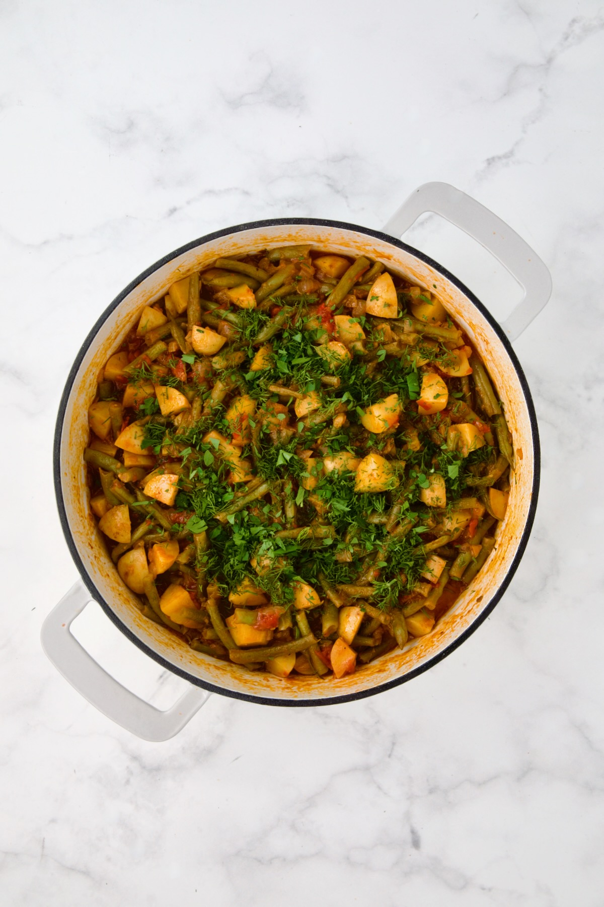 Cooked Fasolakia in white enamel cast iron skillet after herbs added.