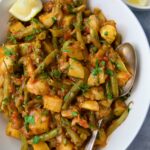 Fasolakia in oval white serving bowl garnished with fresh herbs and lemon wedges.