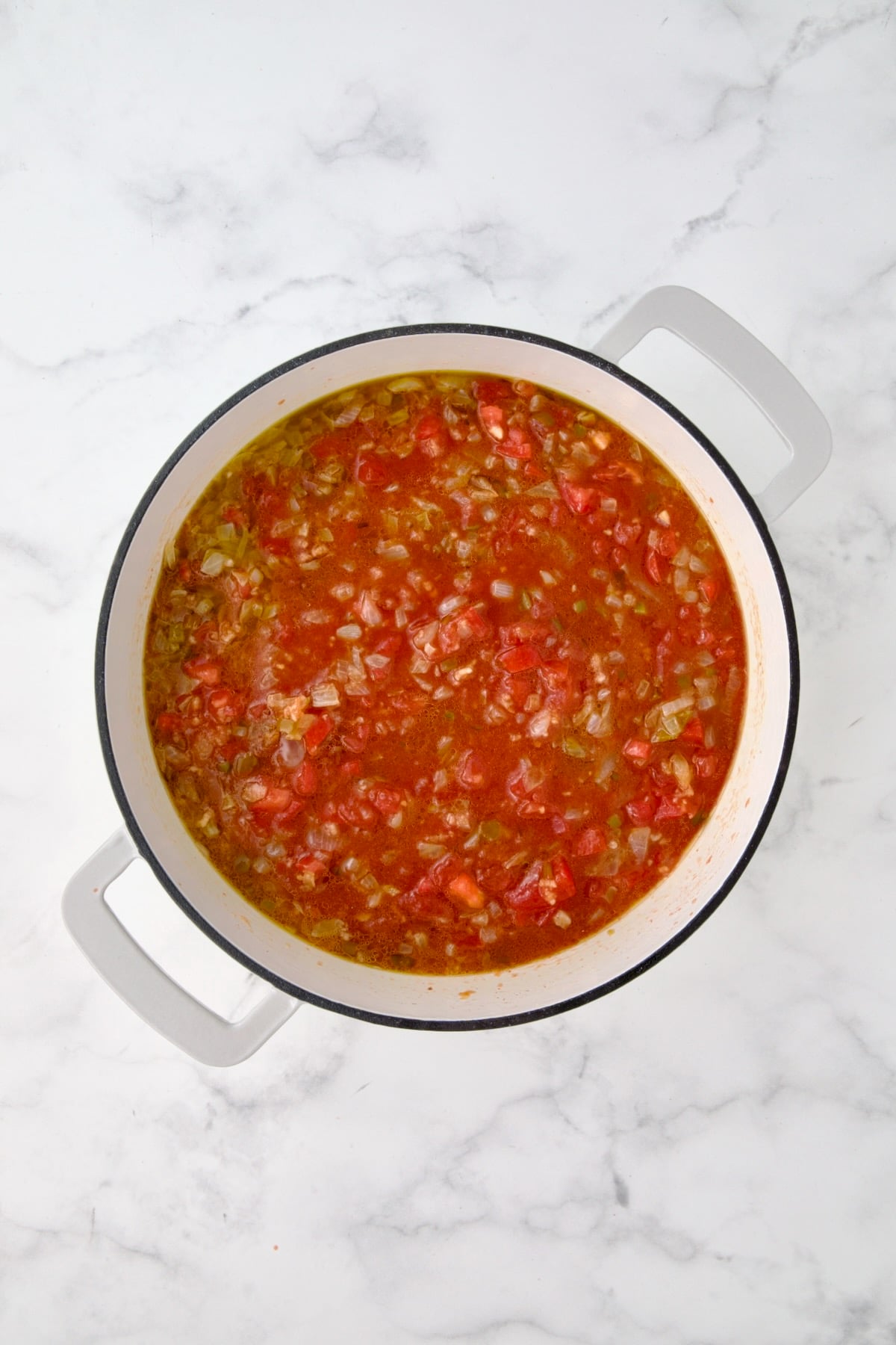 Tomatoes, diced tomatoes and water added to onions, peppers and garlic mixed together in white enamel cast iron skillet.