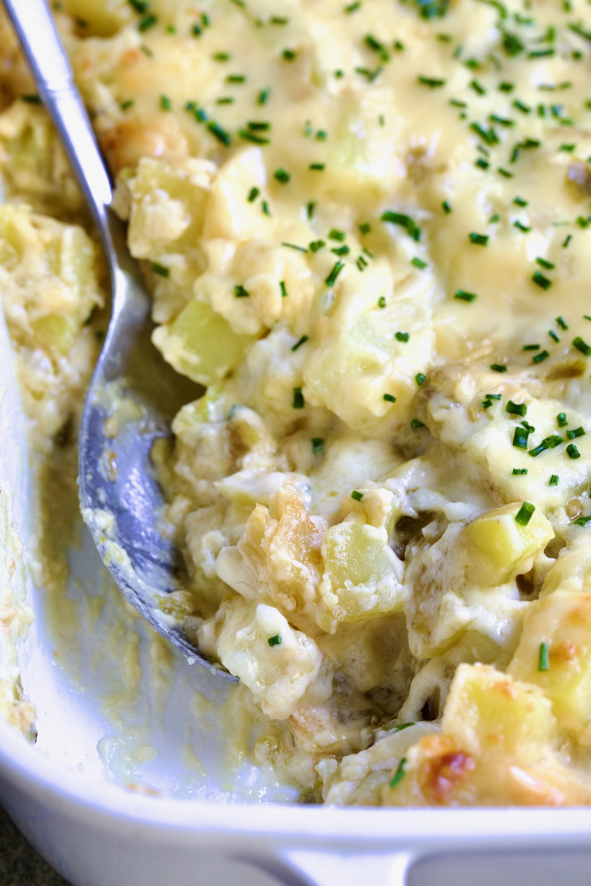 Hatch Green Chile au Gratin Potatoes in white rectangular baking dish with serving spoon scooping some out.