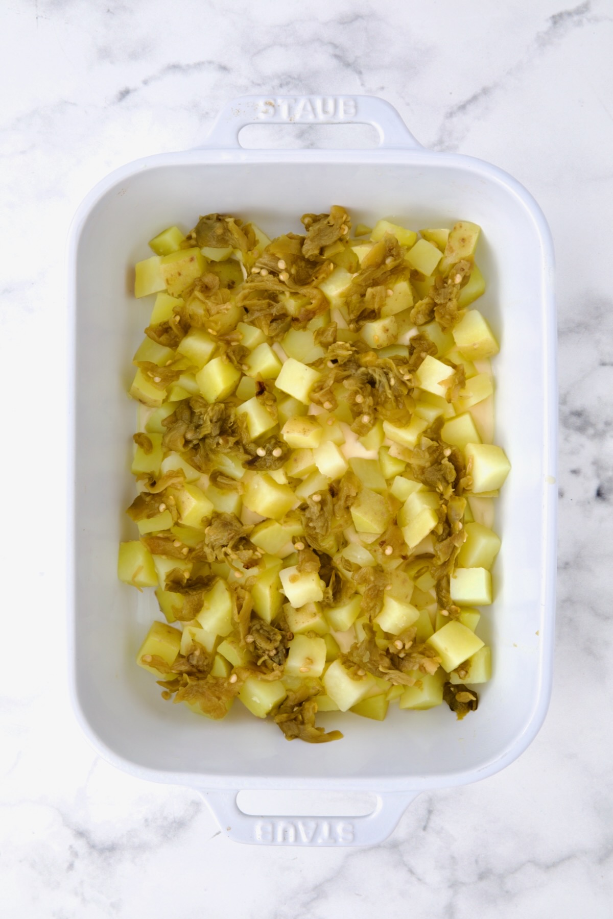 First layer of potatoes and green chiles in white rectangular saucepan.