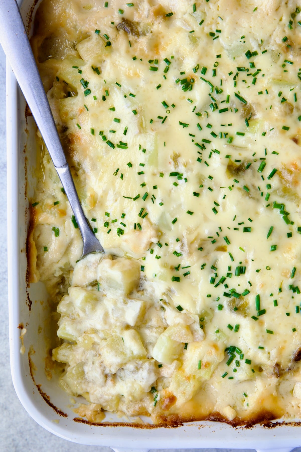 Hatch Green Chile au Gratin Potatoes in white rectangular baking dish with serving spoon scooping some out.