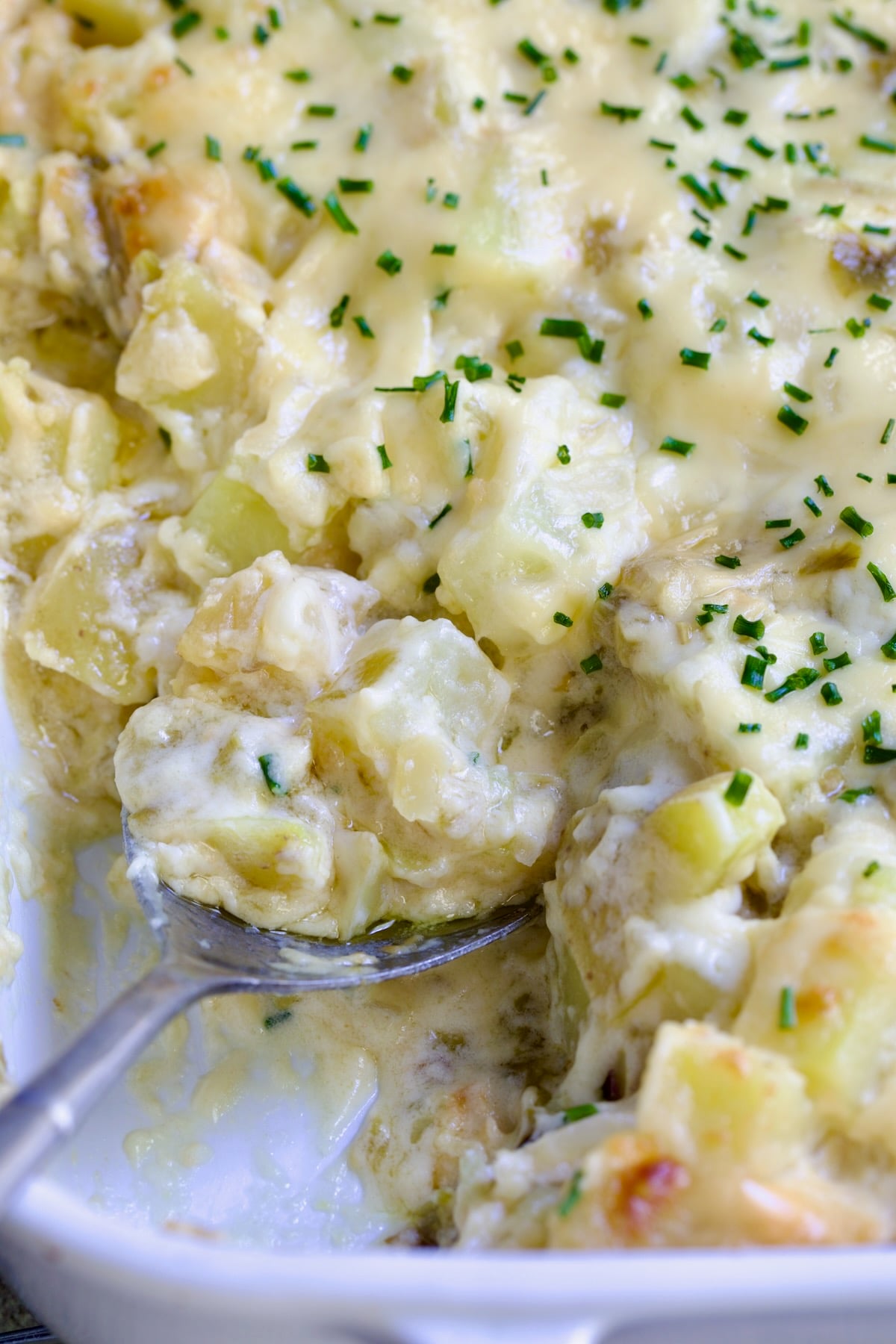 Hatch Green Chile au Gratin Potatoes in white rectangular baking dish with serving spoon scooping some out.
