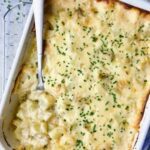 Hatch Green Chile au Gratin Potatoes in white rectangular baking dish with serving spoon scooping some out.