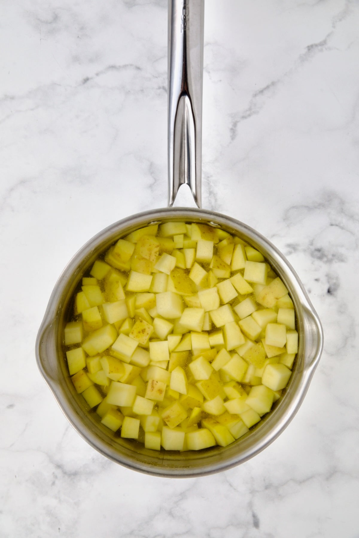 Cubed potatoes in water in stainless steel saucepan before being cooked.