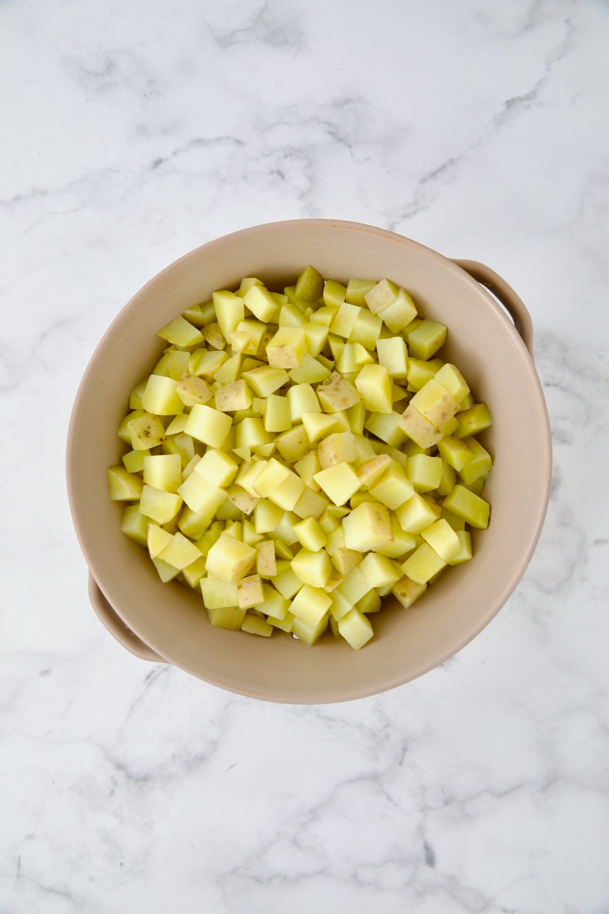 Cooked cubed potatoes in beige colander.