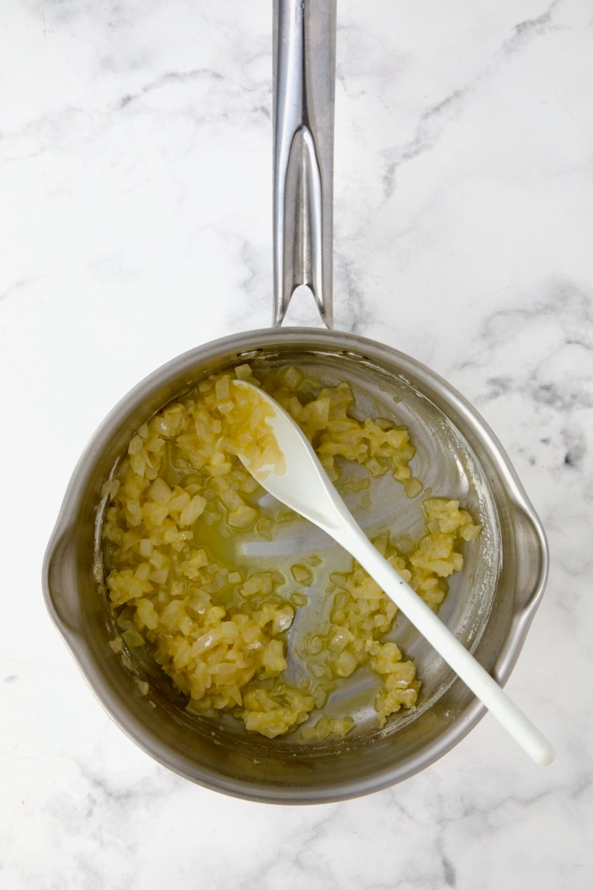 Flour added to cooked onions in butter and oil in stainless steel saucepan being stirred with white spoon.