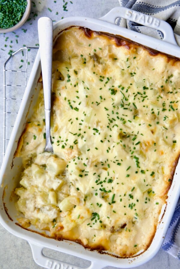 Hatch Green Chile au Gratin Potatoes in white rectangular baking dish with serving spoon scooping some out.