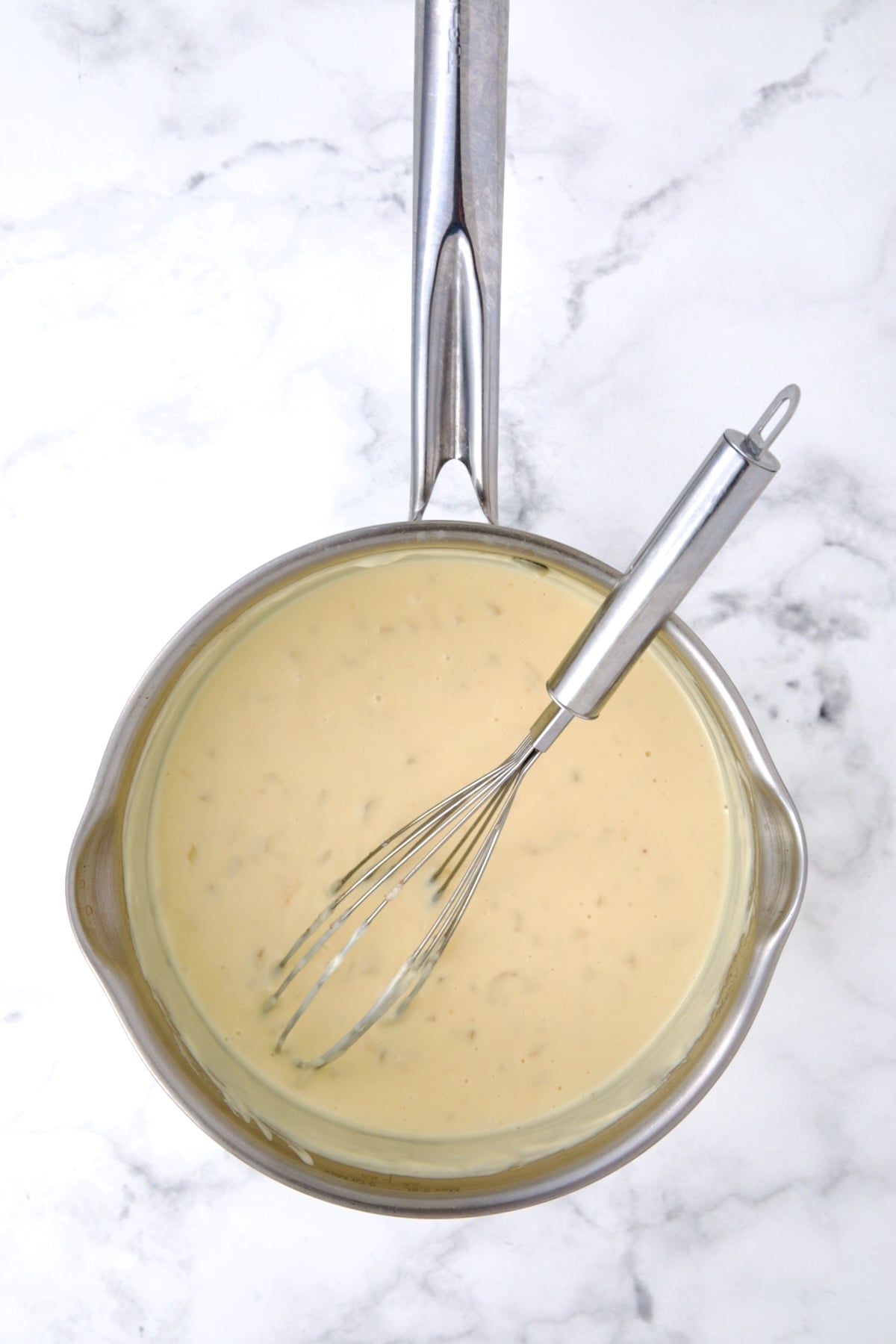 Cheese sauce in stainless steel saucepan with wire whisk.
