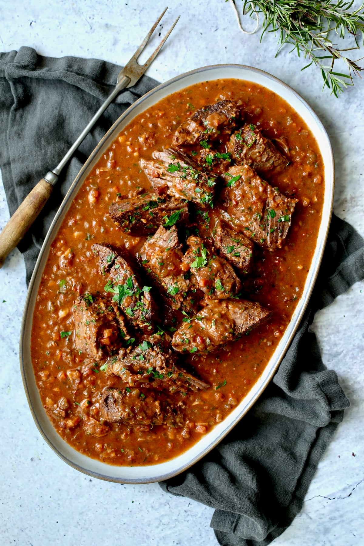 Italian Pot Roast (Stracotto) broken into pieces on oval gray-rimmed platter with meat fork.