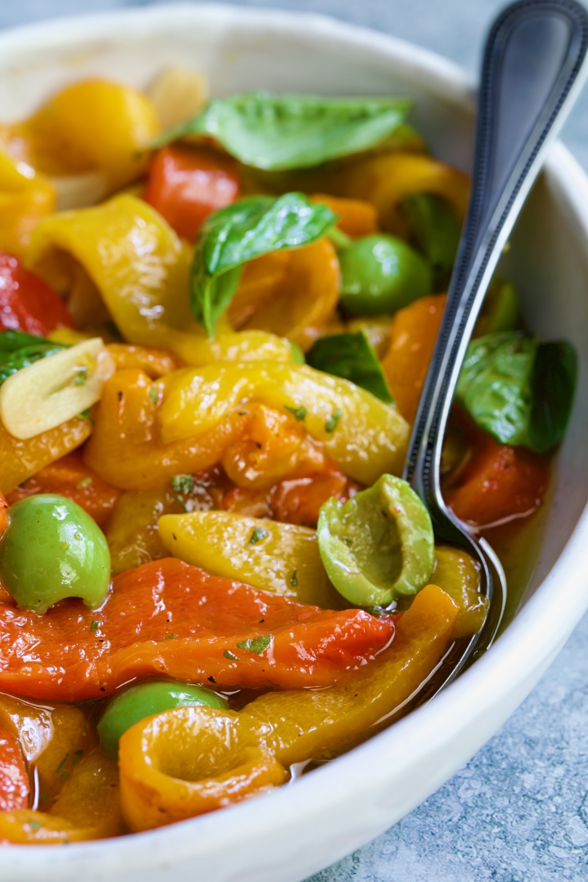 Roasted Pepper Salad in white oval serving bowl with serving spoon garnished with fresh basil leaves.