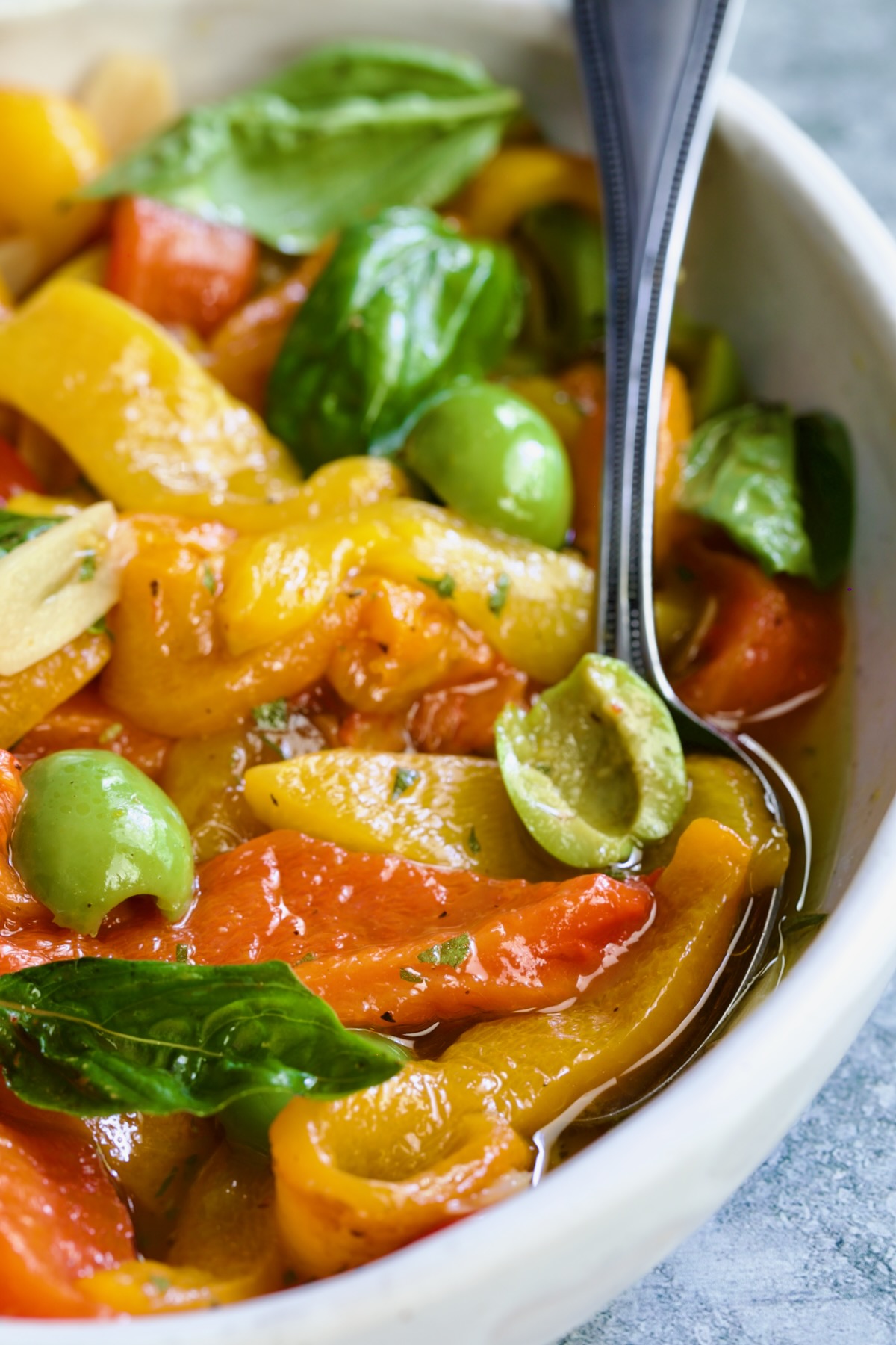 Roasted Pepper Salad in white oval serving bowl with serving spoon garnished with fresh basil leaves.