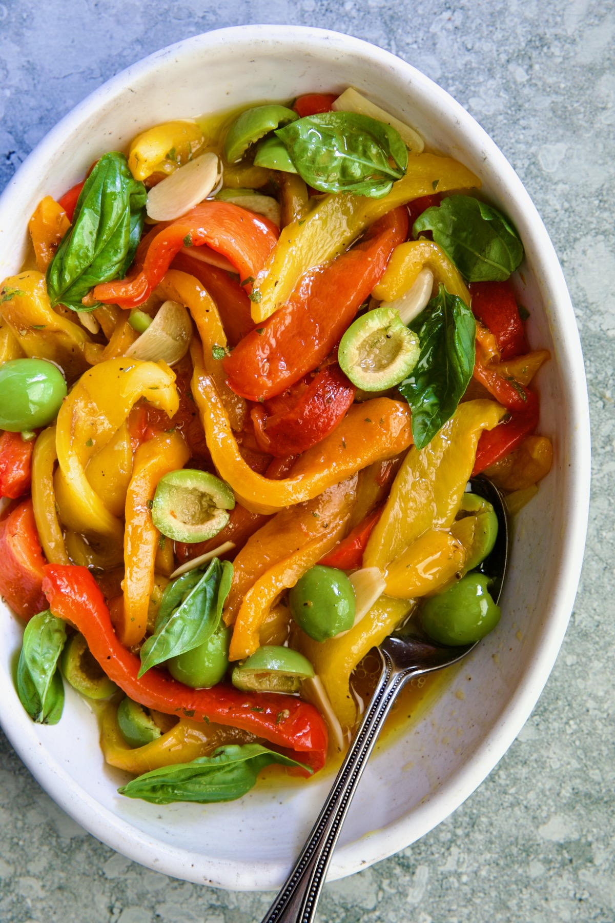 Roasted Pepper Salad in white oval serving bowl with serving spoon garnished with fresh basil leaves.