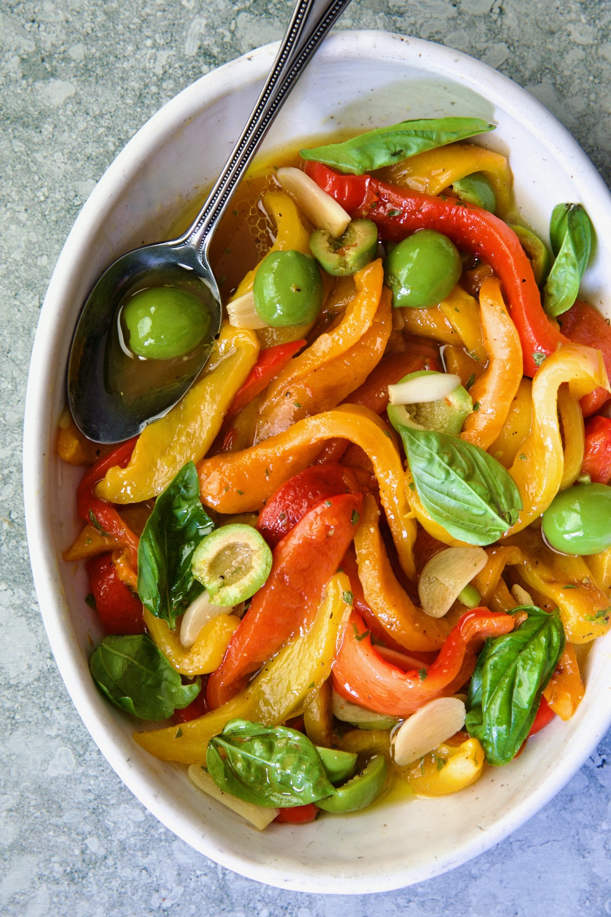 Roasted Pepper Salad in white oval serving bowl with serving spoon garnished with fresh basil leaves.