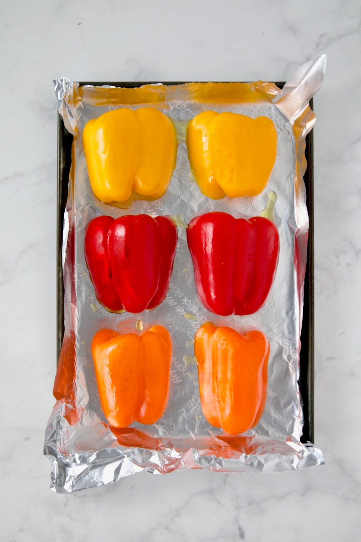 Yellow, red and orange bell pepper halves on aluminum foil-lined rimmed sheet pan with garlic halves under them.