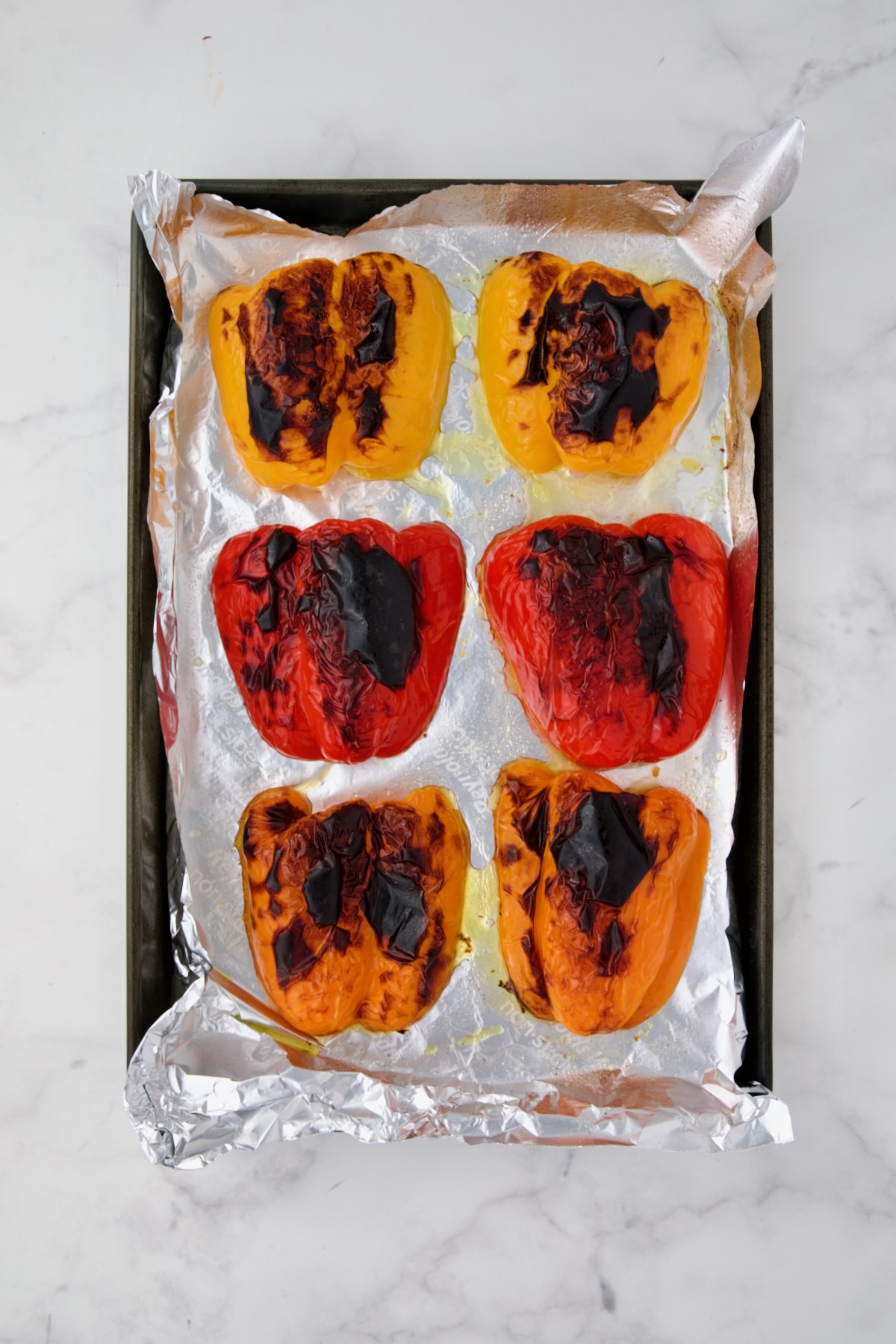 Charred yellow, red and orange bell pepper halves on aluminum foil-lined rimmed baking sheet.