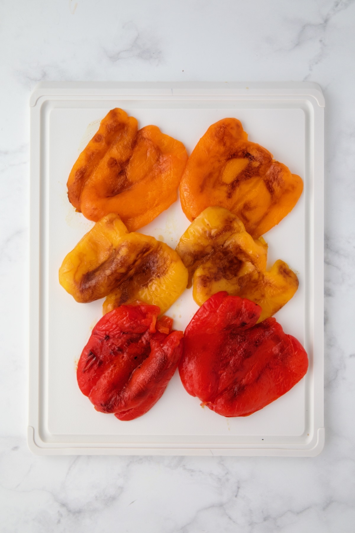 Skinned orange, yellow and bell pepper halves on white plastic cutting board.