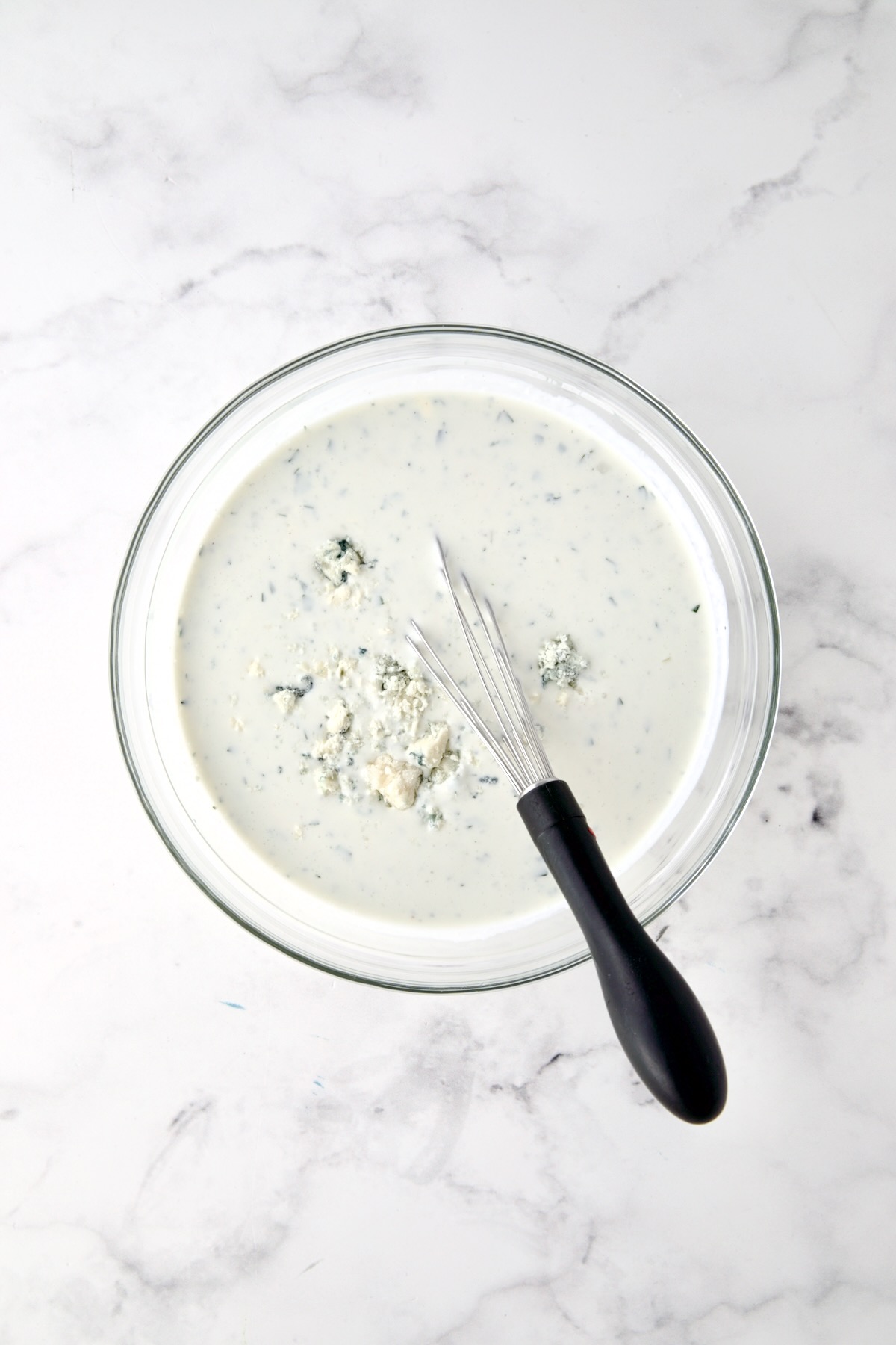 Blue cheese dressing in glass bowl with wire whisk.