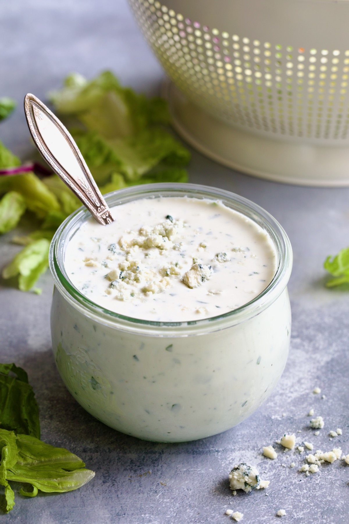 Best Blue Cheese Dressing Recipe in glass jar with spoon and lettuce in the background.