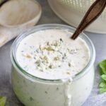 Best Blue Cheese Dressing Recipe in glass jar with spoon and colander in the background.