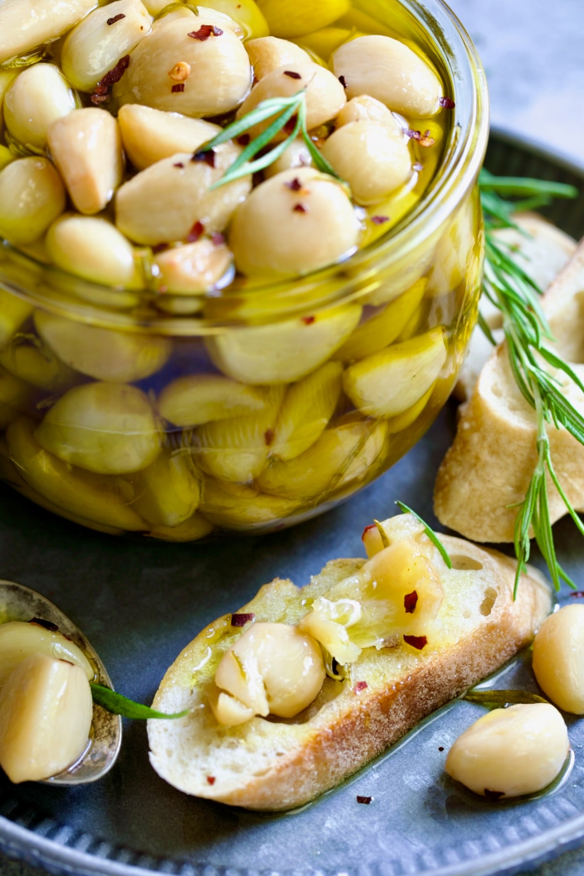 Garlic Confit in glass jar with cloves of garlic mashed on a piece of bread.