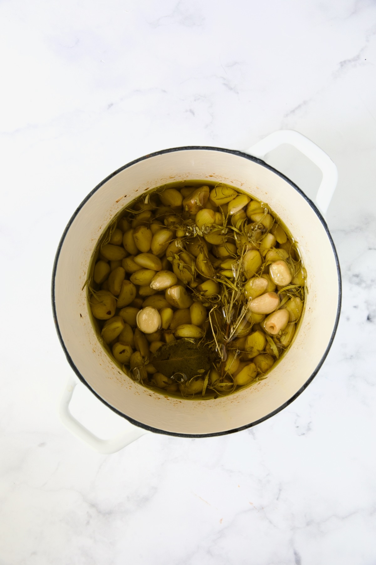 Ingredients for Garlic Confit in white Dutch oven after being simmered.