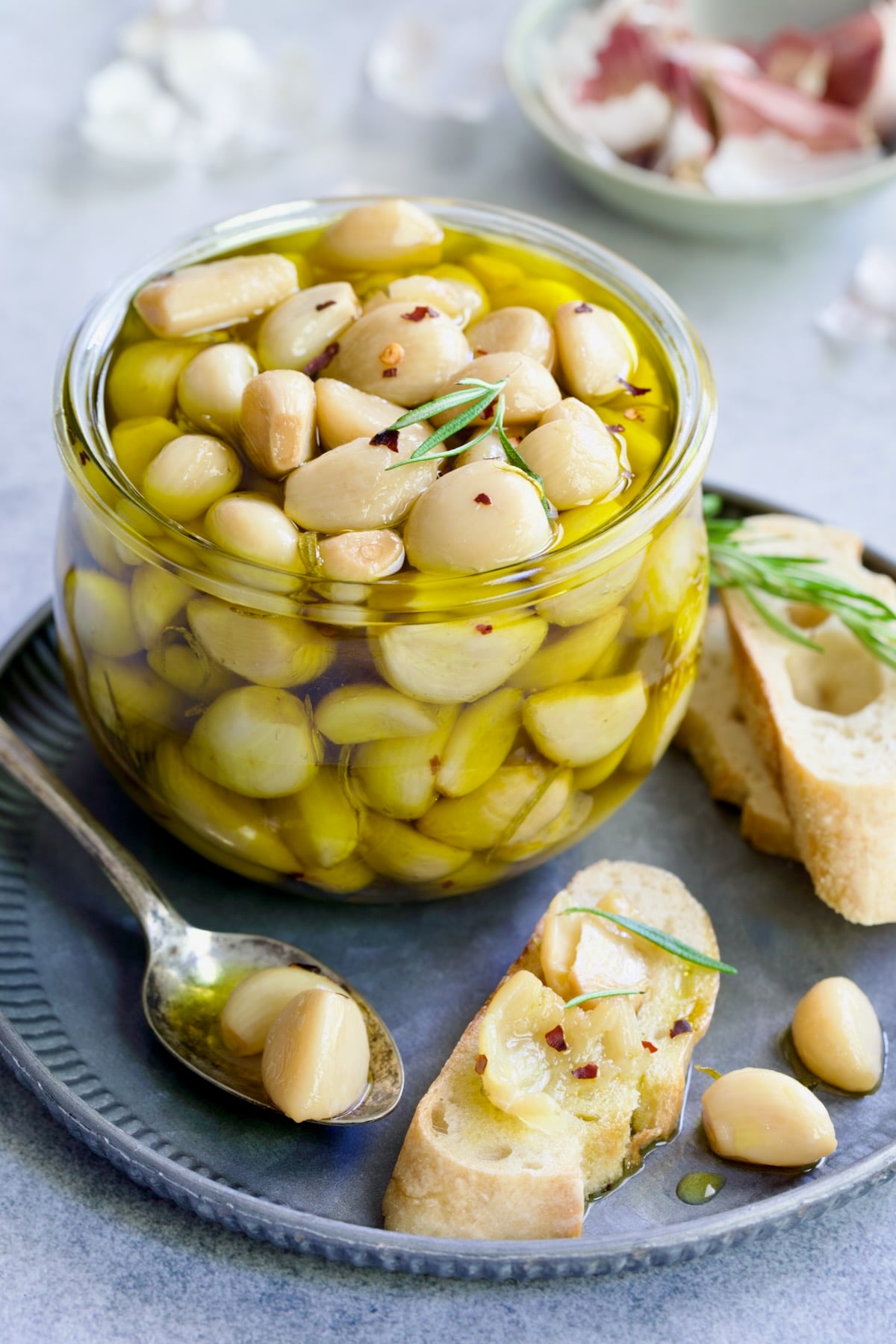 Garlic Confit in glass jar with cloves of garlic mashed on a piece of bread.