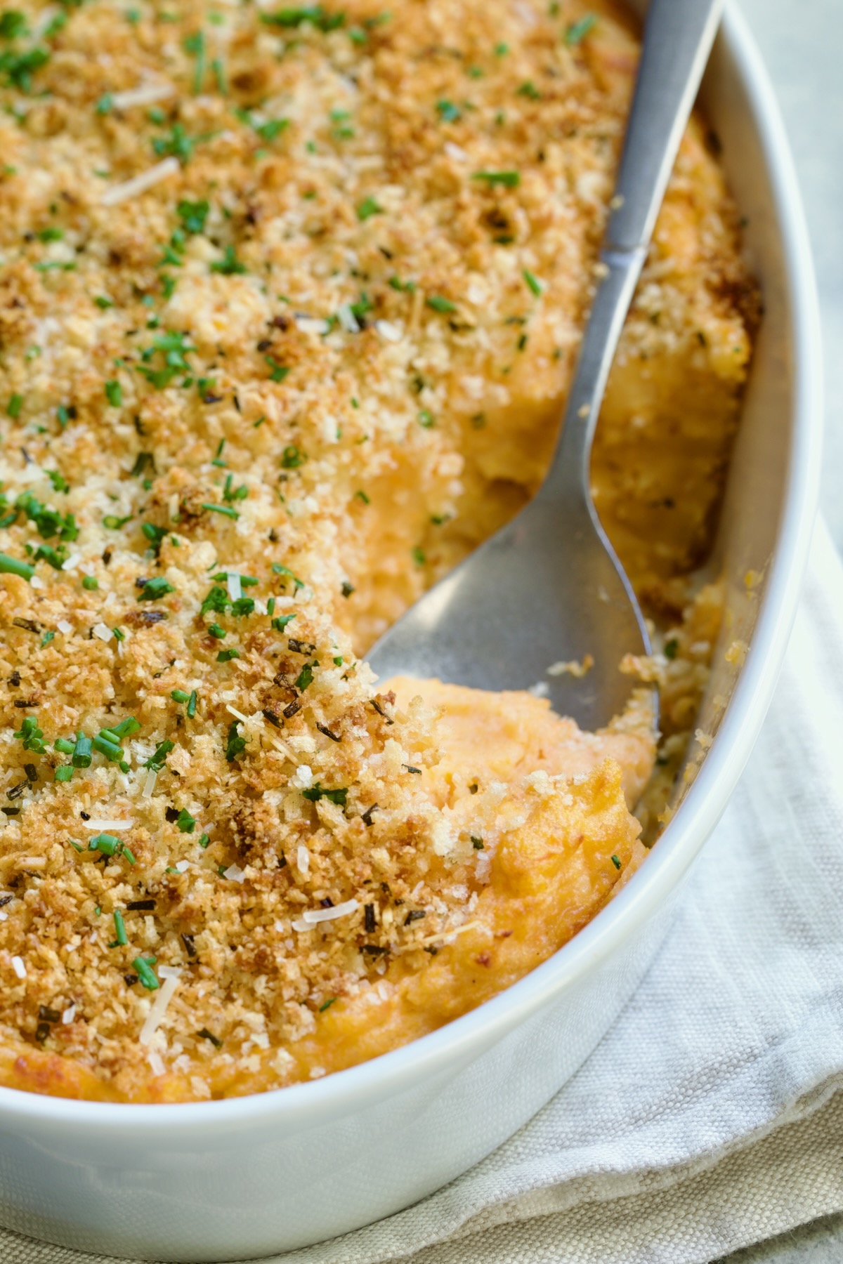 Potato and Sweet Potato Bake in white oval baking dish with silver spoon scooping some out.