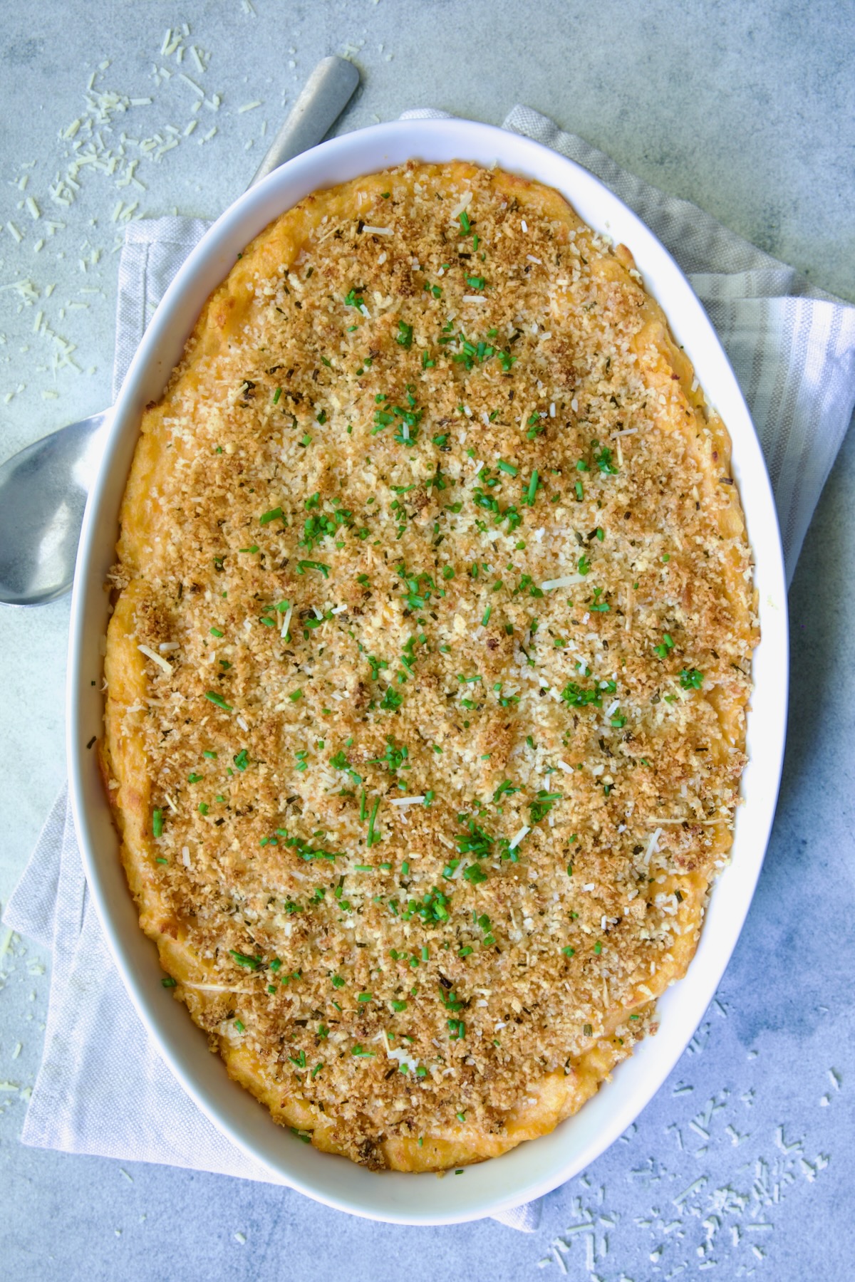 Potato and Sweet Potato Bake in white oval baking dish with silver serving spoon.