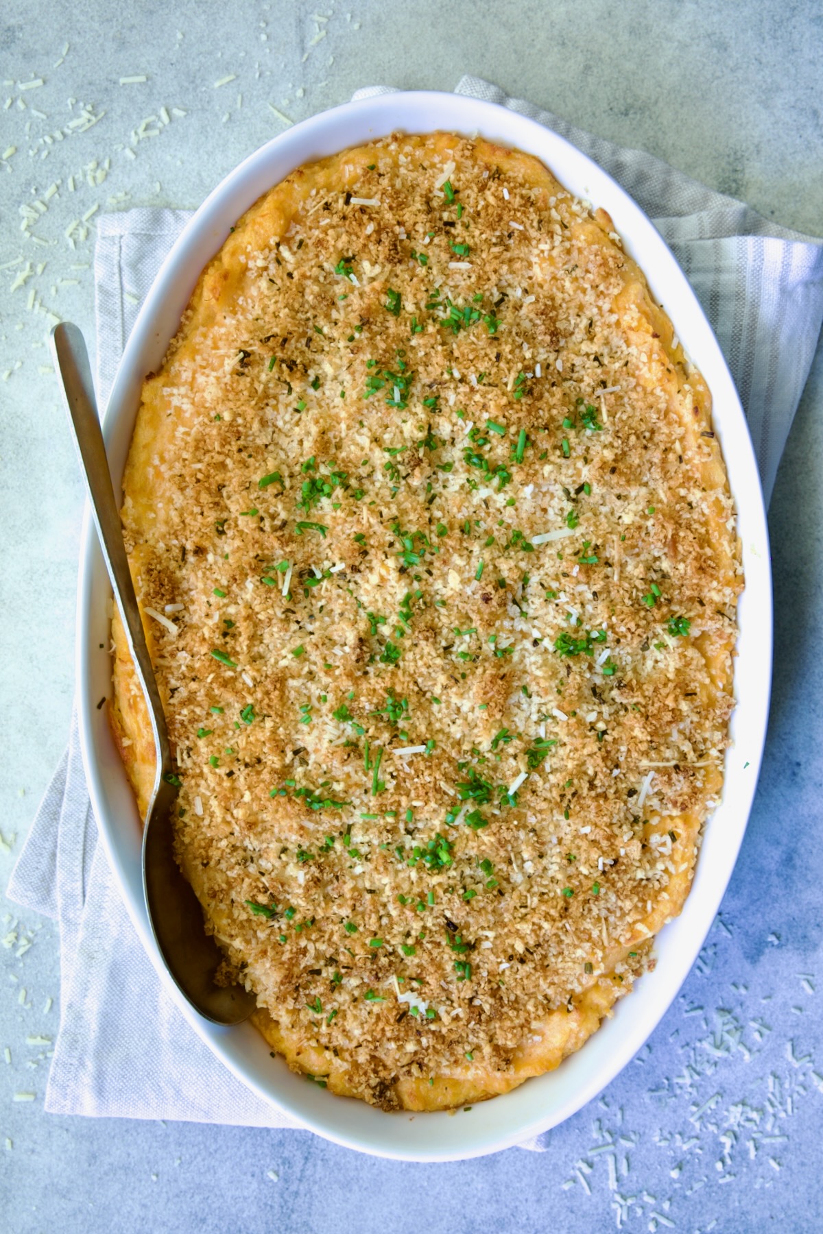 Potato and Sweet Potato Bake in white oval baking dish with silver serving spoon.