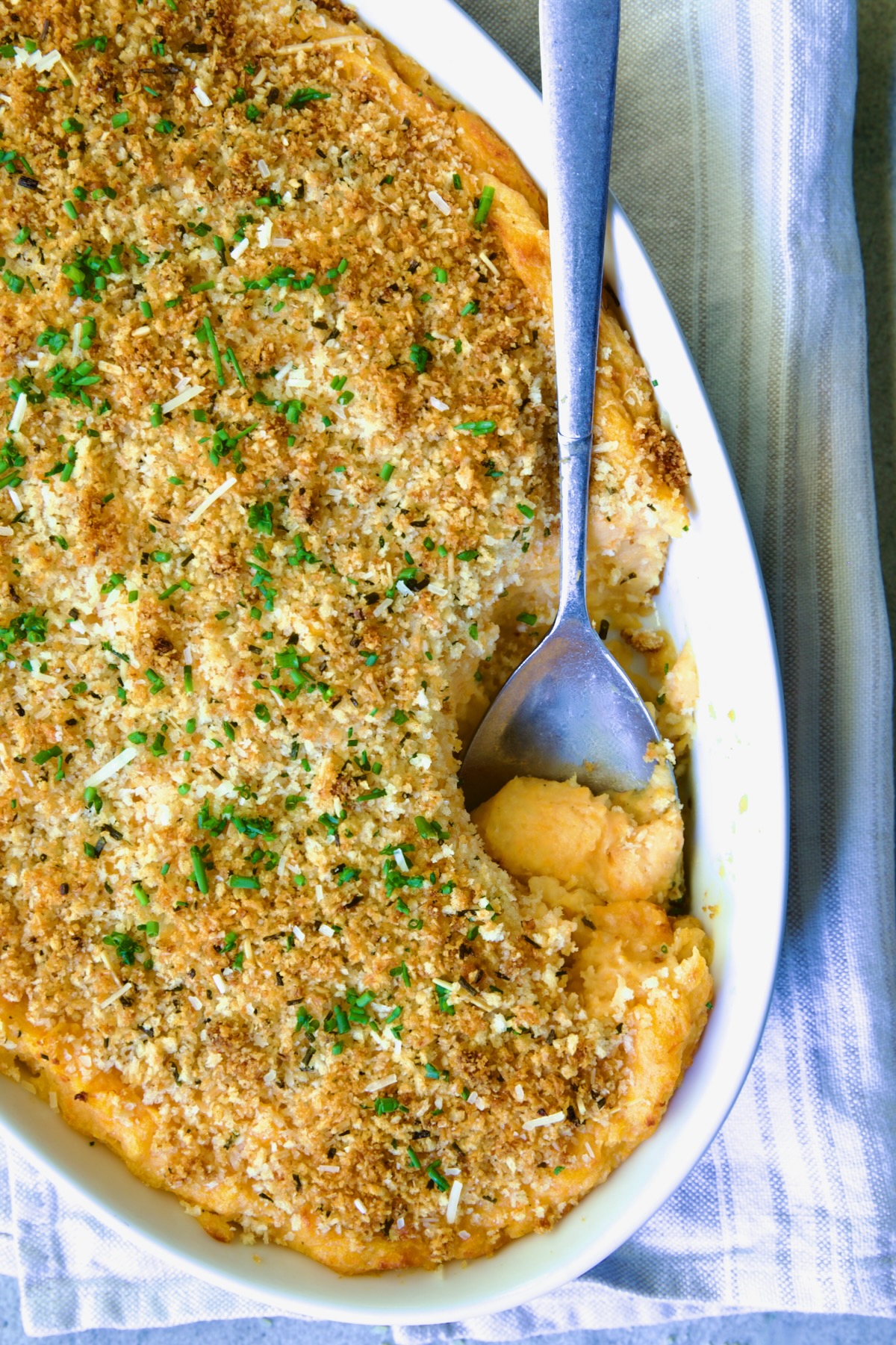 Potato and Sweet Potato Bake in white oval baking dish with silver spoon scooping some out.
