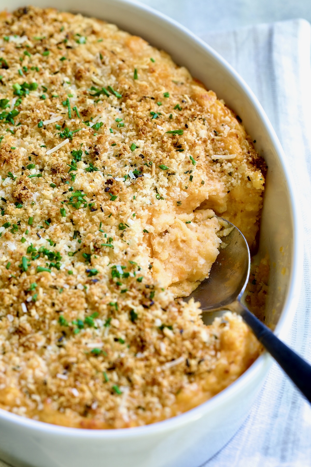 Potato and Sweet Potato Bake in white oval baking dish with silver spoon scooping some out.