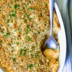 Potato and Sweet Potato Bake in white oval baking dish with silver spoon scooping some out.