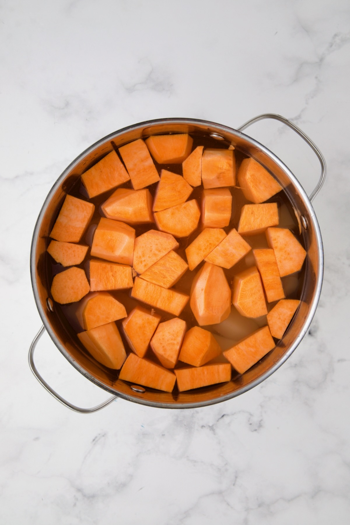 Russets and sweet potatoes in water in stainless steel pot before being cooked.