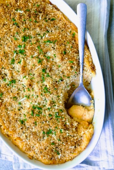 Potato and Sweet Potato Bake in white oval baking dish with silver spoon scooping some out.