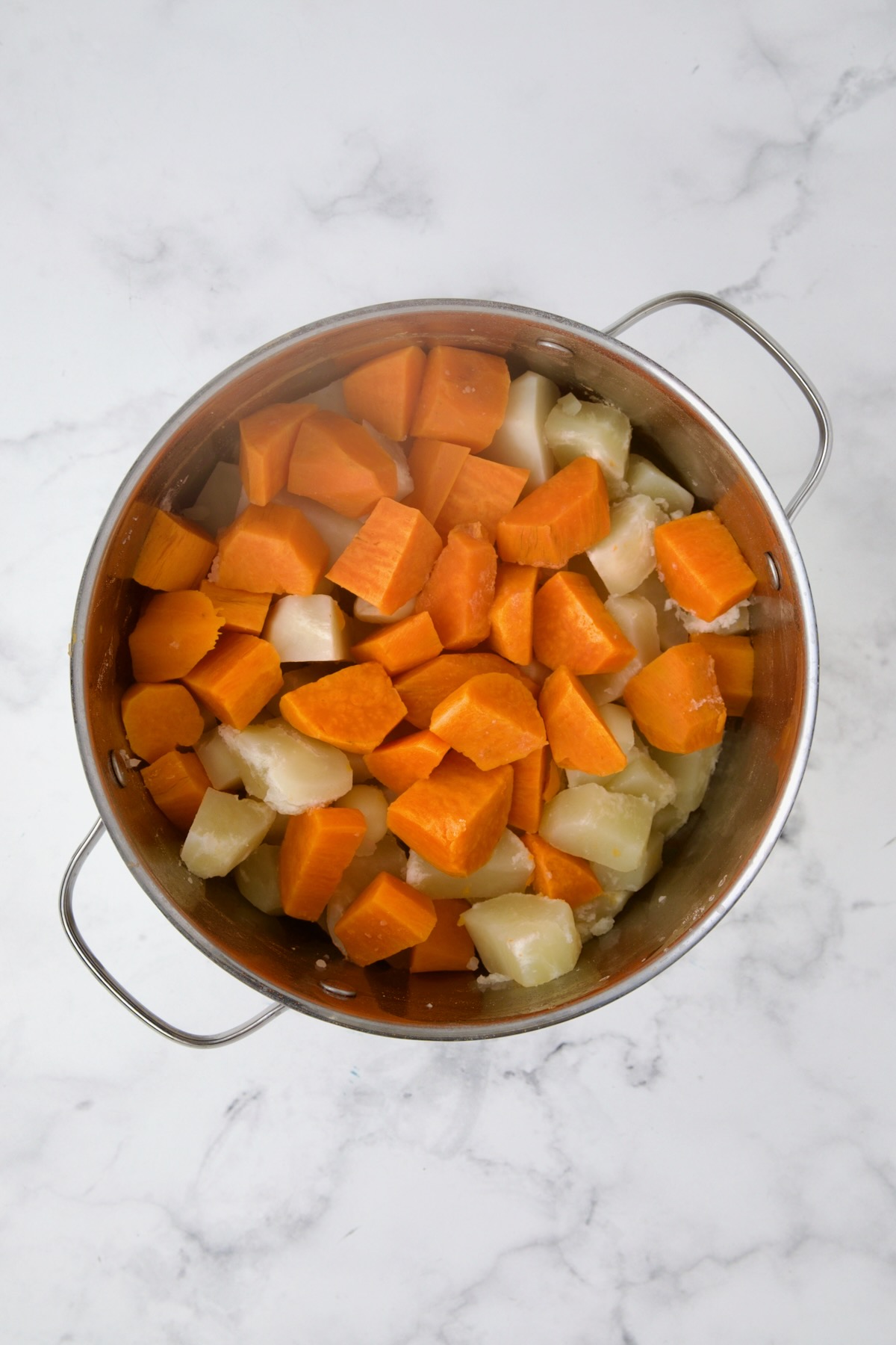 Drained Russets and sweet potatoes in stainless steel pot after being cooked.