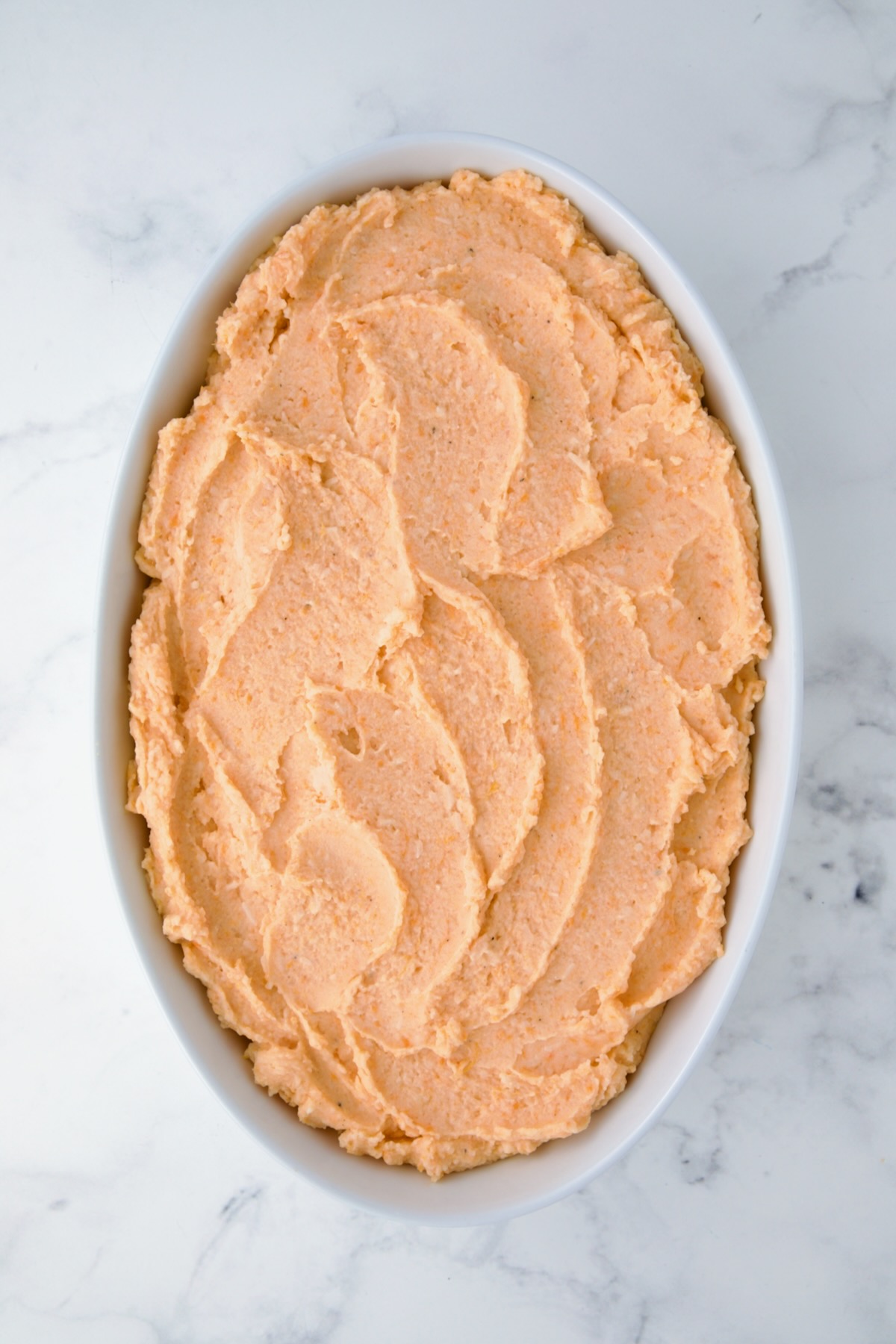 Potato and Sweet Potato Bake in white oval baking dish before topping is added and before being baked.