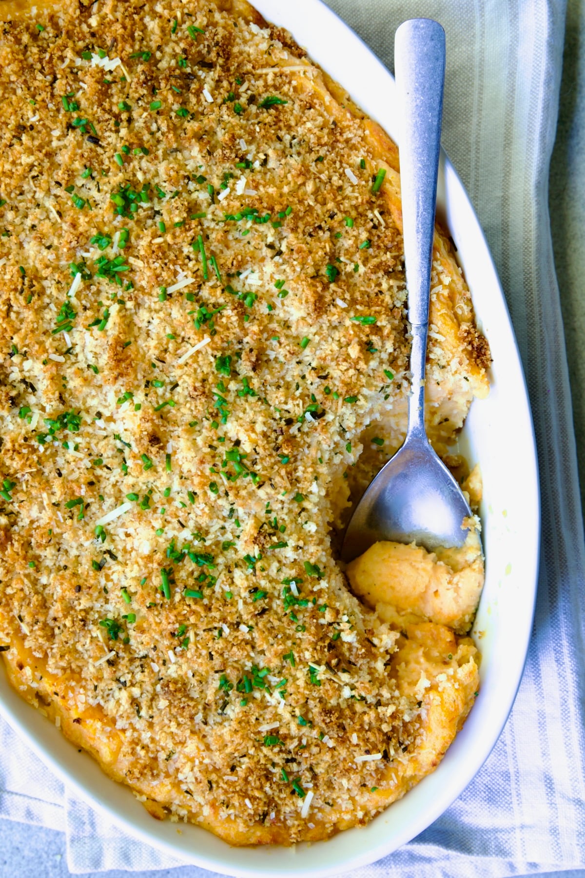 Potato and Sweet Potato Bake in white oval baking dish with silver spoon scooping some out.