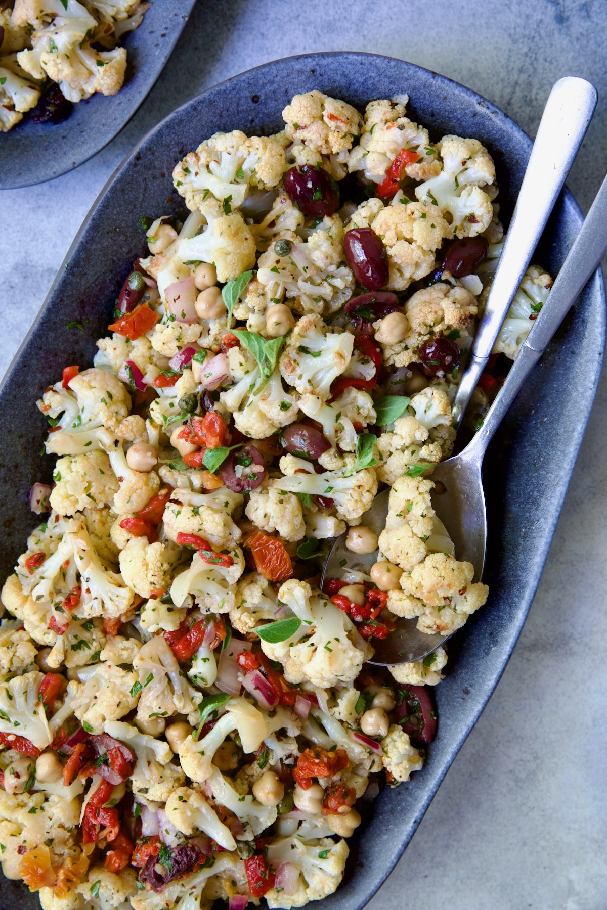Roasted Cauliflower Salad on gray speckled platter with serving utensils.