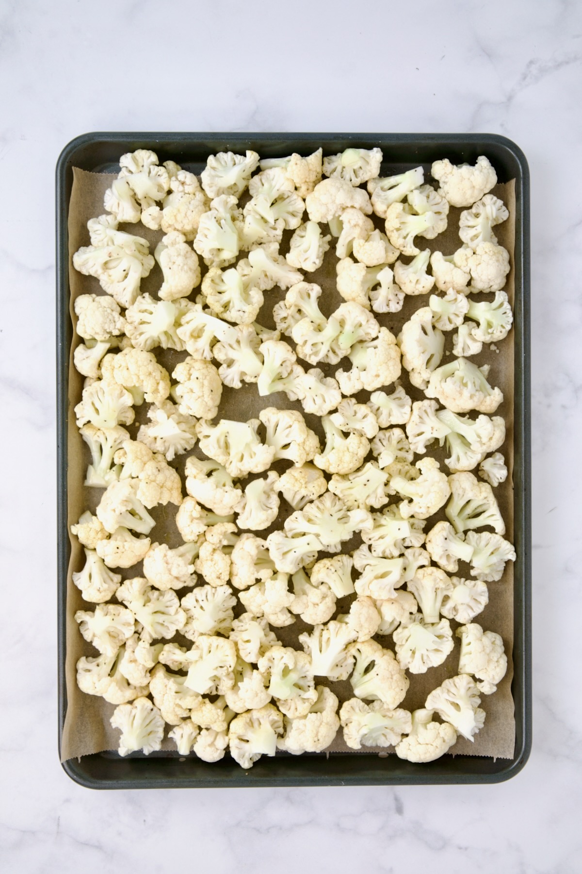 Uncooked cauliflower on parchment paper lined baking sheet.