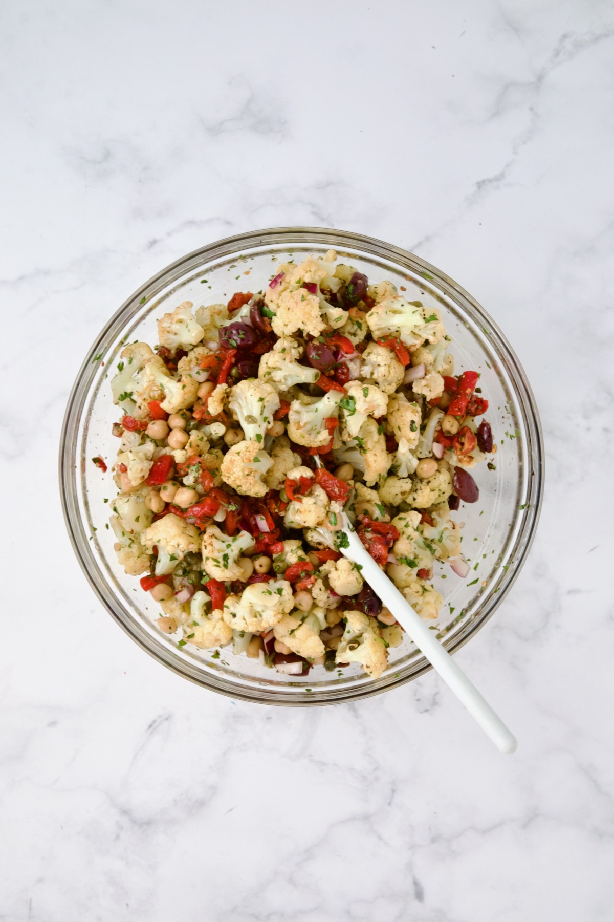 Ingredients for cauliflower salad in glass bowl with cauliflower added after being combined.